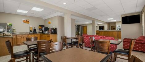 A spacious dining area with wooden tables and chairs, a kitchen in the background, and a ceiling fan.