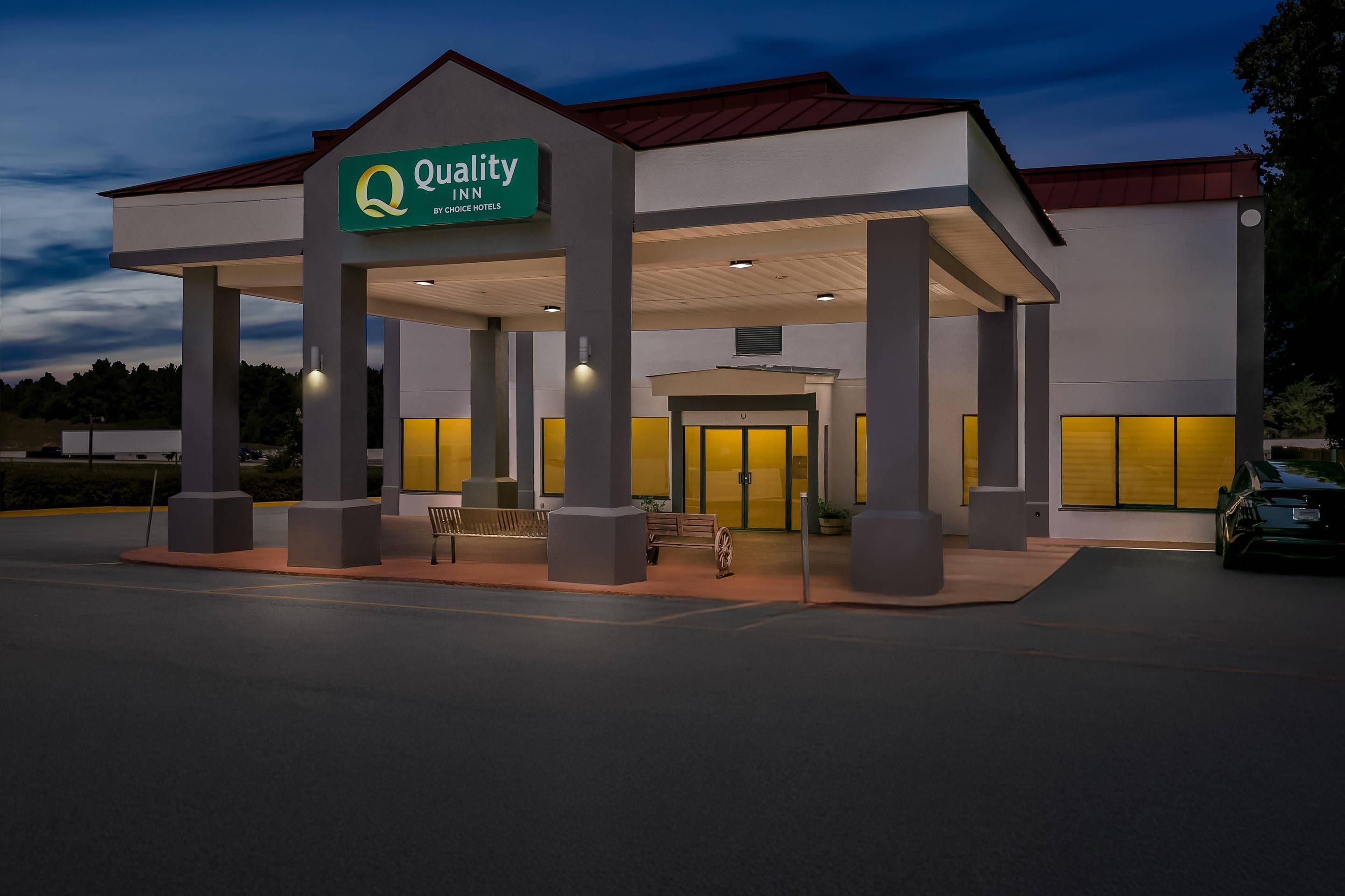 A hotel with a covered entrance, outdoor seating, and a sign indicating it is a Quality Inn by Choice Hotels.