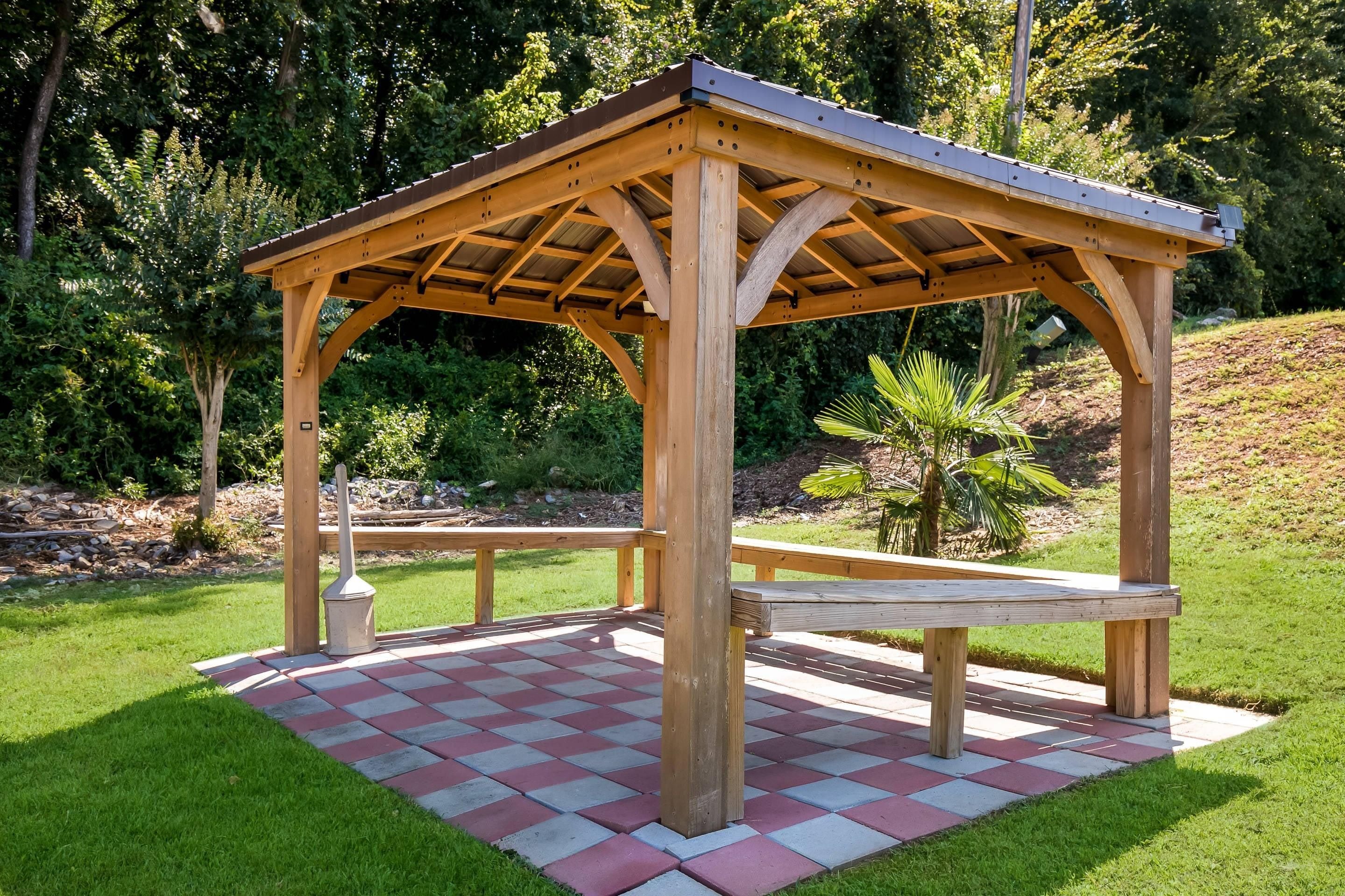 Un kiosque en bois doté d’un sol à carreaux, entouré de verdure.