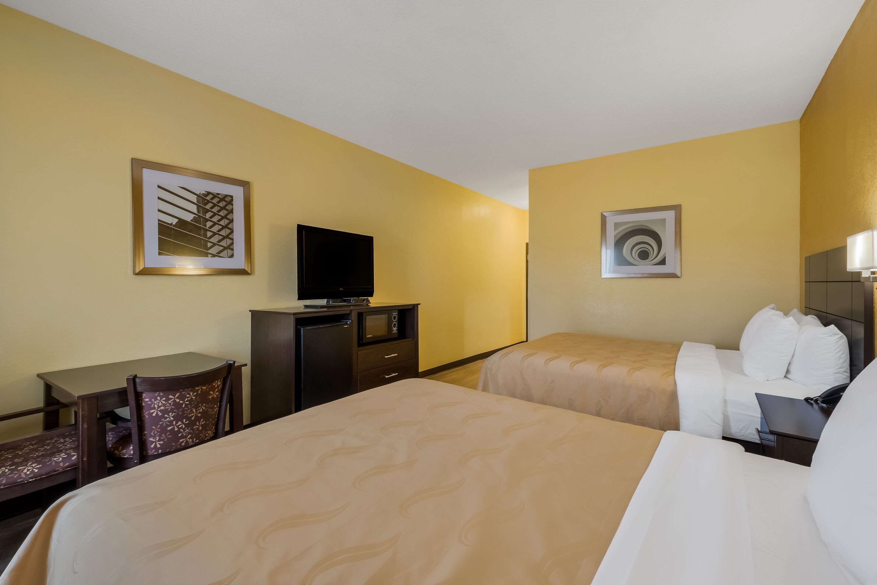 Una habitación de hotel con dos camas, un escritorio, un televisor y obras de arte en las paredes.