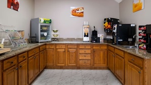 Una cocina con armarios de madera, una cafetera, un fabricante de gofres y una bandeja de frutas.