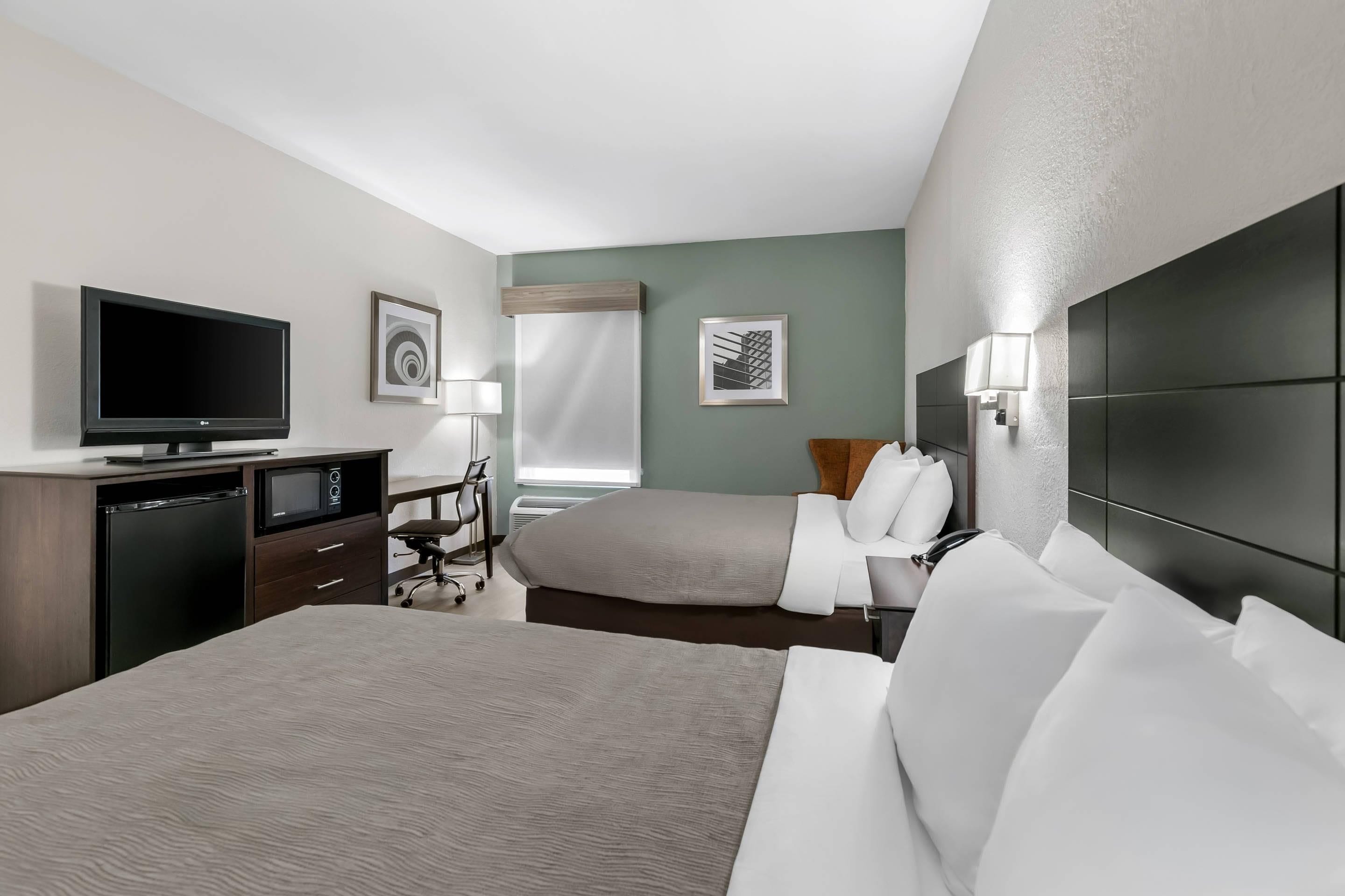Habitación de hotel con cama, escritorio con televisor, una silla, lámpara de escritorio y dos cuadros en la pared.
