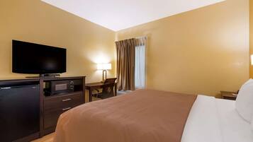 A hotel room with a bed, a desk with a lamp, a television, and a mini-fridge.