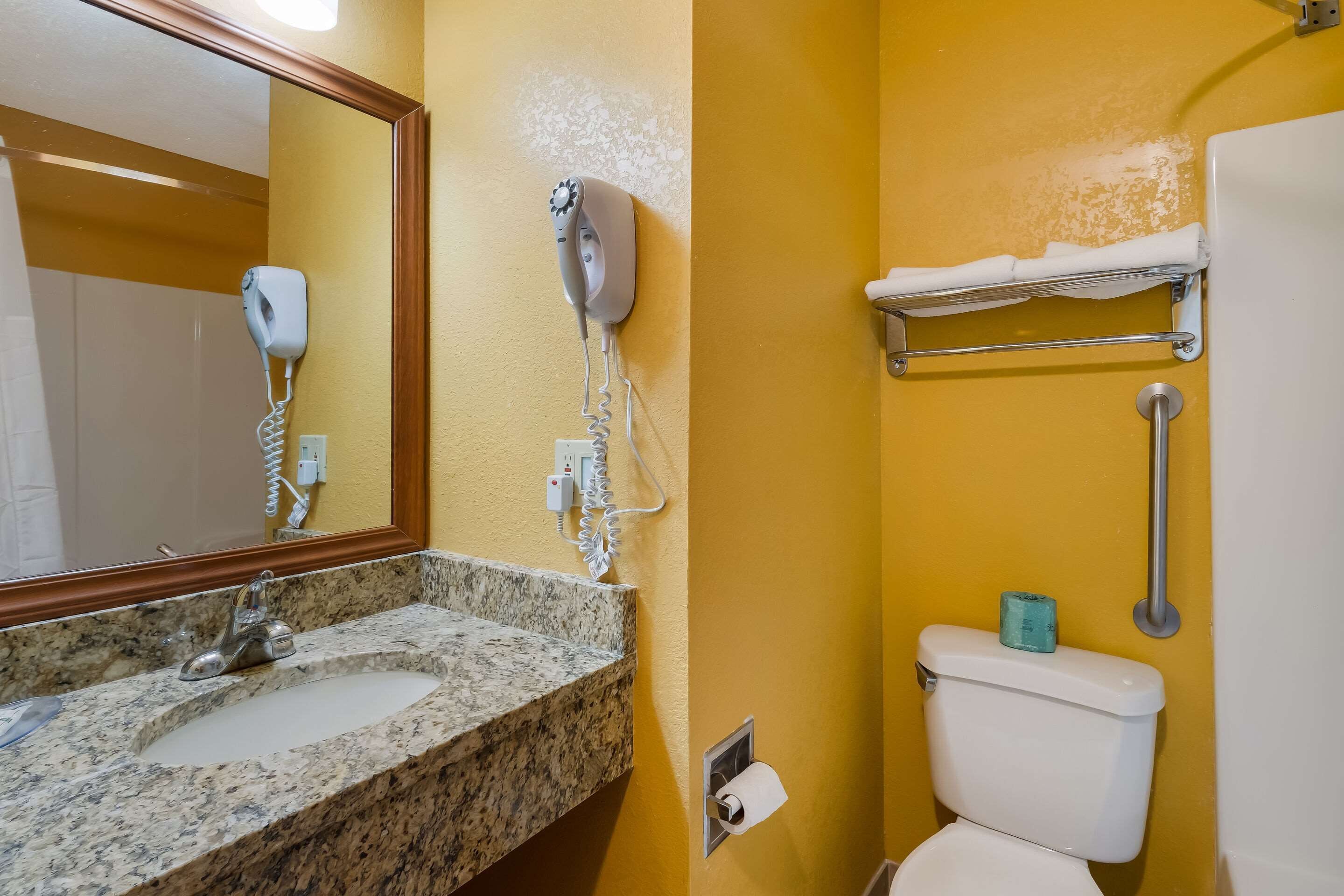 Un baño con lavamanos de granito, un secador de pelo, inodoro y un perchero para toallas.