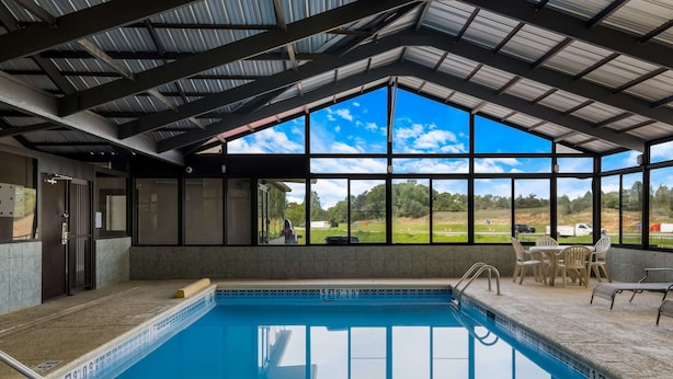 Una piscina interior con vistas despejadas al exterior, una zona de estar cubierta y una estructura de techo metálico.