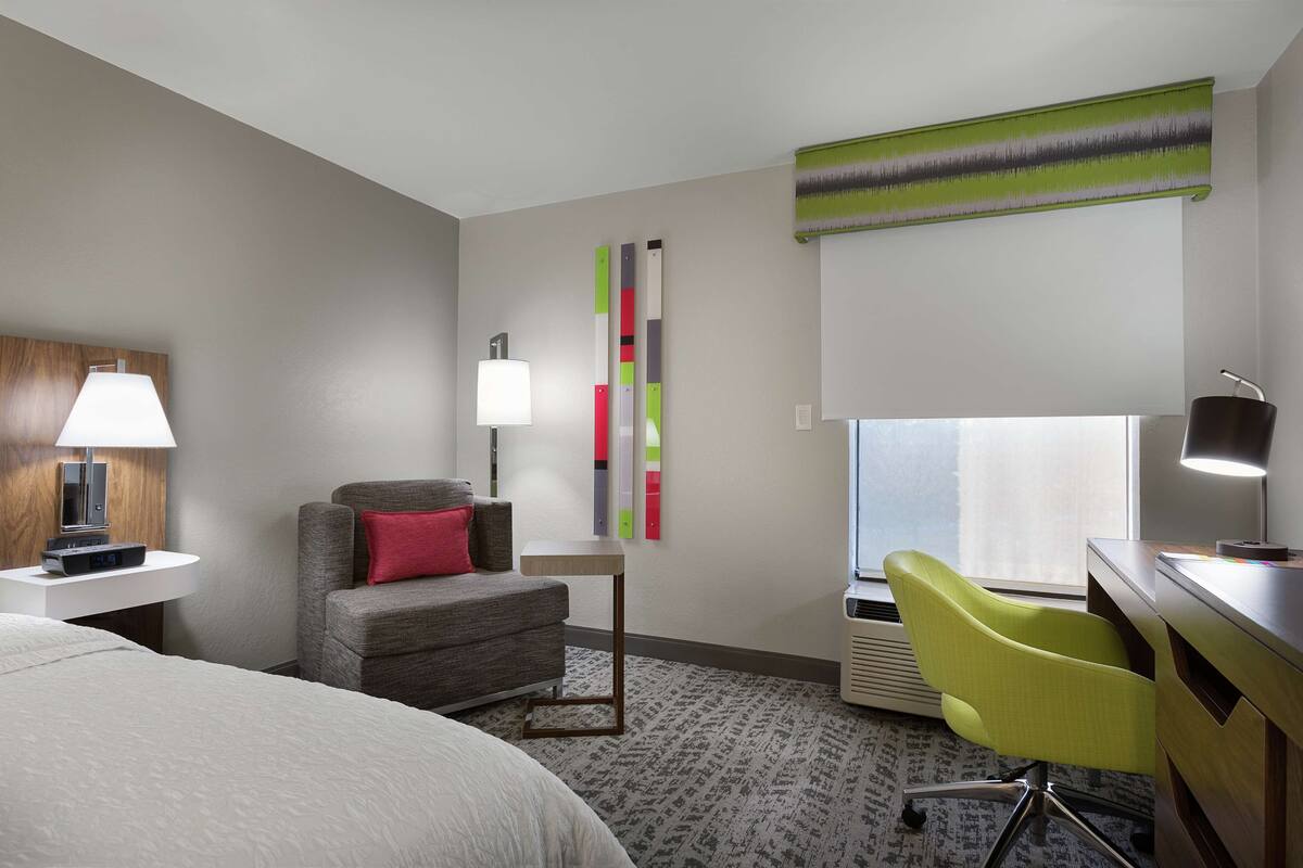 Ein Hotelzimmer mit Bett, Schreibtisch, Stuhl, Lampe, Fernseher und Fenster.