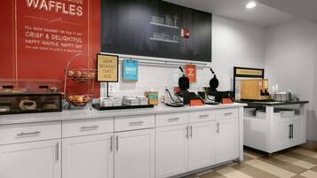 Uma cozinha limpa e moderna, com armários brancos, estação de waffles e diversos eletrodomésticos.