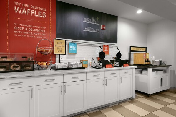 A clean, modern kitchen with white cabinets, a waffle station, and various kitchen appliances.
