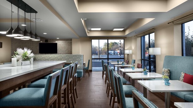En moderne restaurant med en lang disk, flere siddeområder og store vinduer der giver udsigt til omgivelserne.