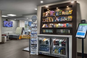 Uma área de conveniência com petiscos embalados, um refrigerador de bebidas abastecido e um quiosque digital.