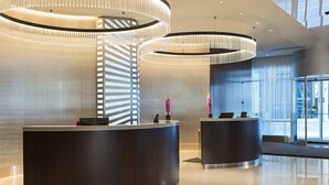 A modern reception area with two curved reception desks, a large glass window, and a contemporary light fixture. - Hotel Chicago Downtown, Autograph Collection by Marriott (Chicago)