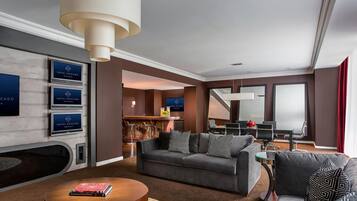 A modern hotel lobby with a grey sofa, a coffee table, and a fireplace. There are signs for the hotel and a reception desk in the background.