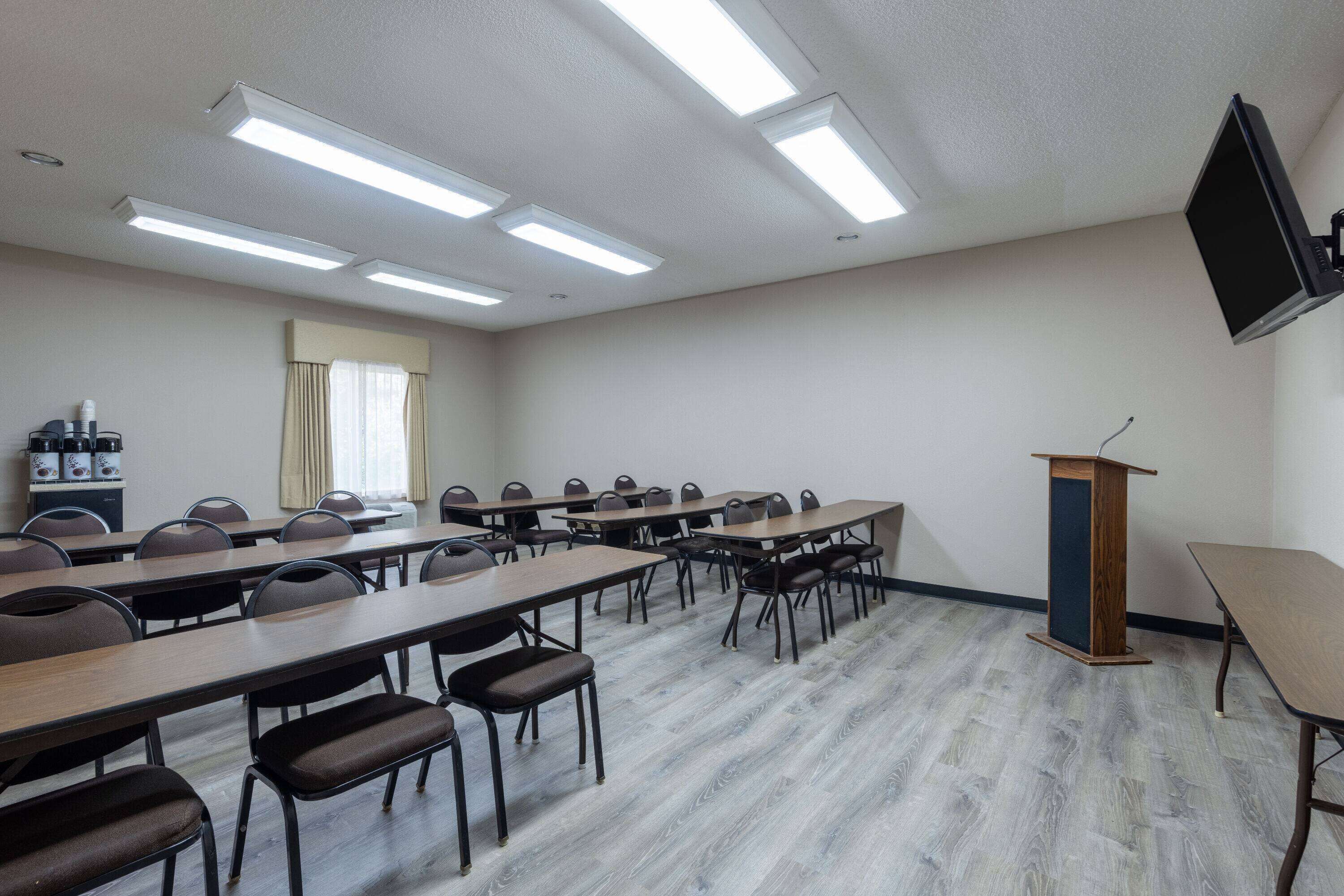 Un salón de conferencias con mesas largas, sillas, un atril y una televisión de pantalla plana en la pared.