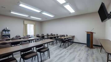Un salón de conferencias con mesas largas, sillas, un atril y una televisión de pantalla plana en la pared.