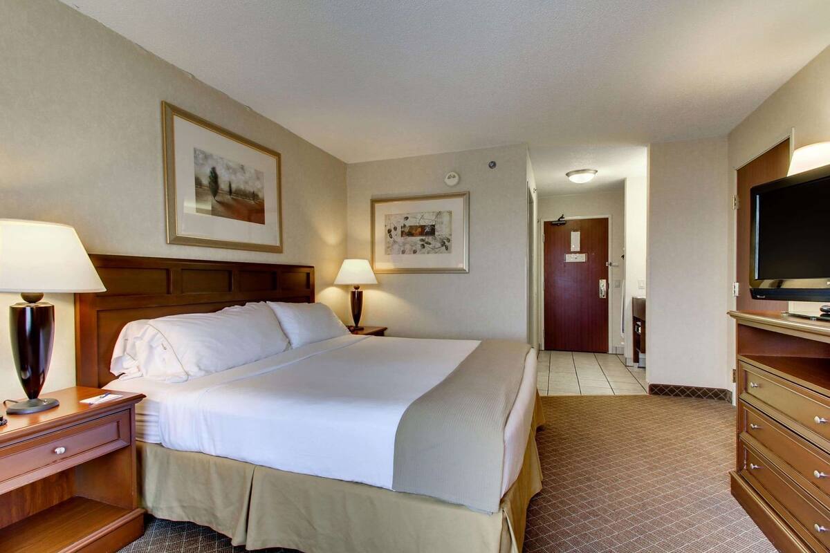 A hotel room with a bed, two bedside lamps, a television, a dresser, and two framed pictures on the wall.