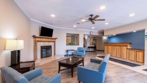 A spacious living area with a fireplace, a ceiling fan, and a reception desk. - Baymont by Wyndham Kirksville University Area (Kirksville)