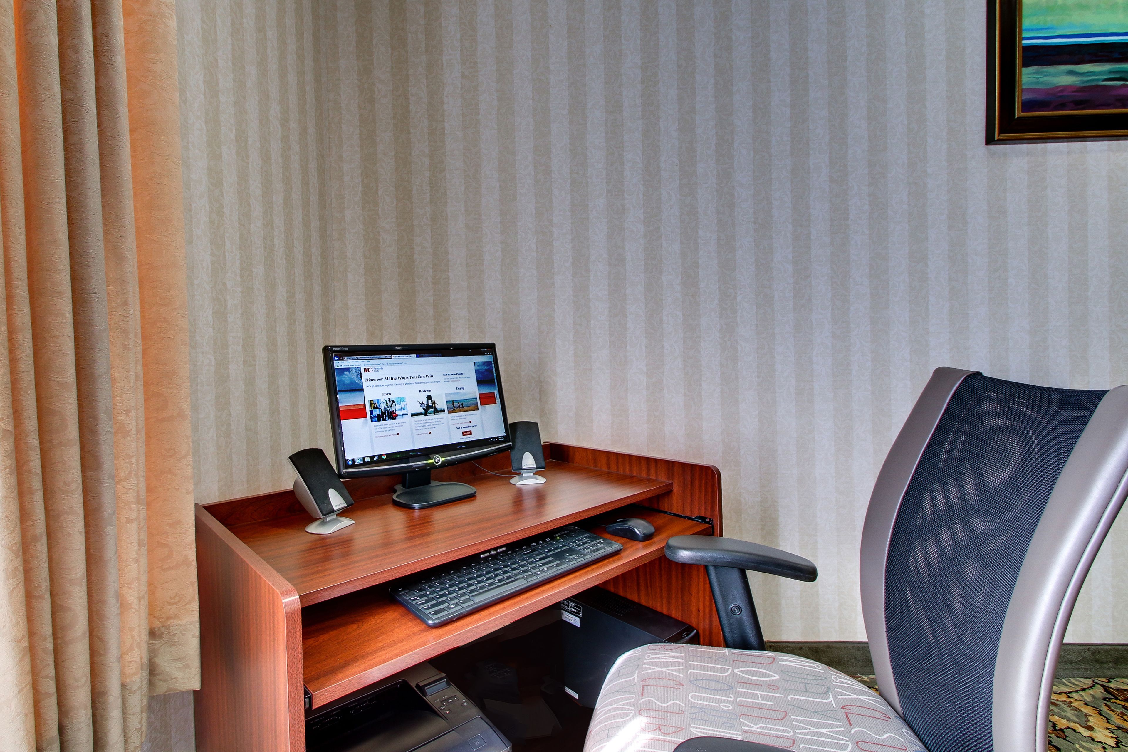 Ein Hotelzimmer mit einem Holztisch, einem Computer, einem Stuhl und einem Fenster mit Vorhängen.