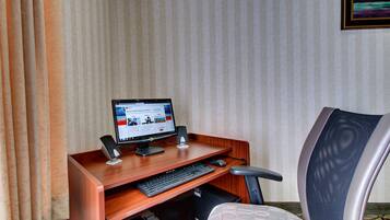A hotel room with a wooden desk, a computer, a chair, and a window with curtains.
