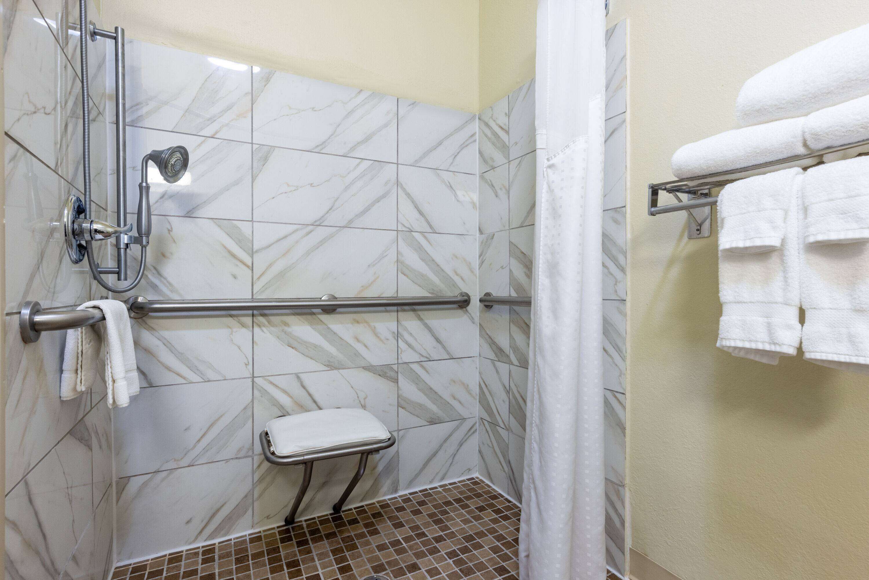 A bathroom with a shower, a grab bar, a white toilet, and a towel rack with towels.