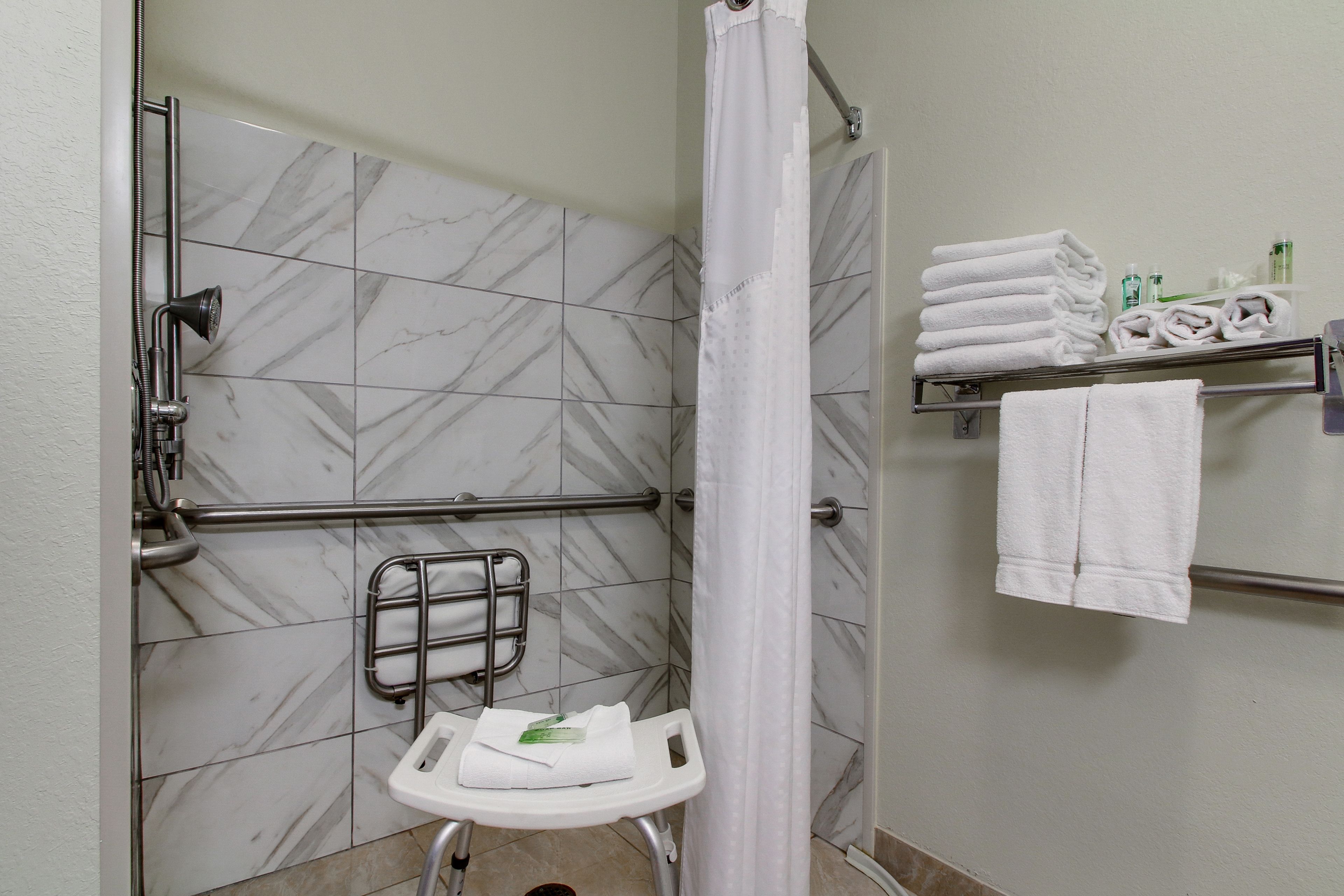 A bathroom with a shower, a toilet, a grab bar, and a towel rack with folded towels.