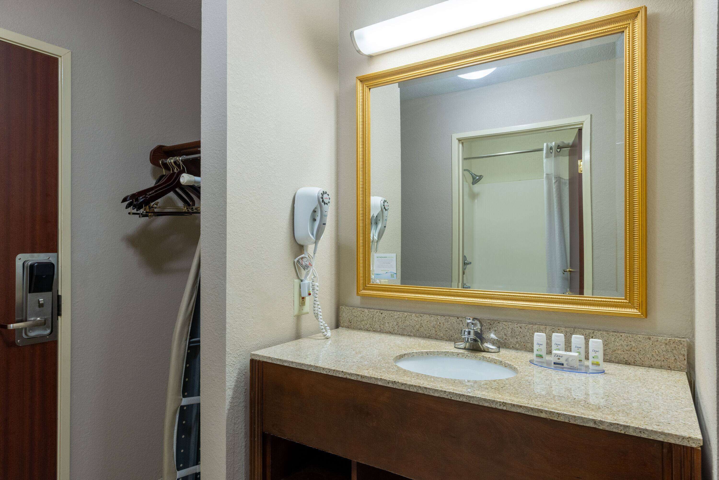 A bathroom with a sink, mirror, towel dispenser, and a shower curtain.