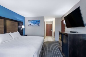 Habitación de hotel con una cama grande, un televisor de pantalla plana montado en la pared, un cabecero de madera y un cuadro en la pared.