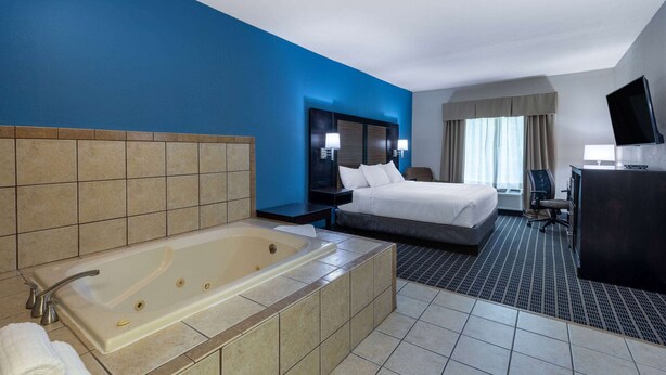 A hotel room with a large bathtub, a bed, a desk, and a television. - Baymont by Wyndham Kirksville University Area (Kirksville)