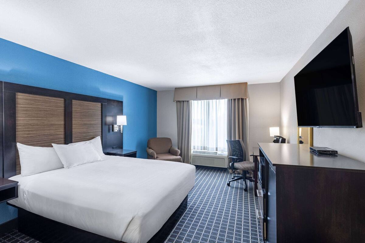 A hotel room with a large bed, a desk, a chair, and a television.