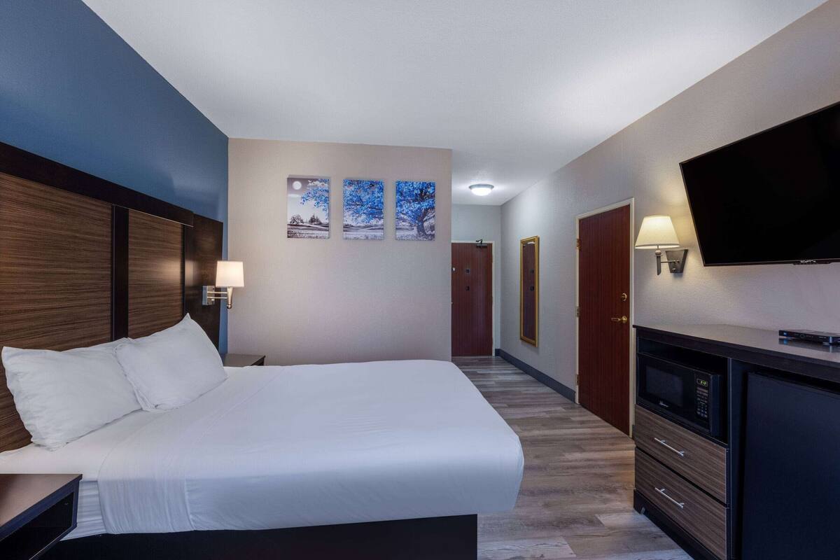 A hotel room with a large bed, a TV, a desk, and a dresser.