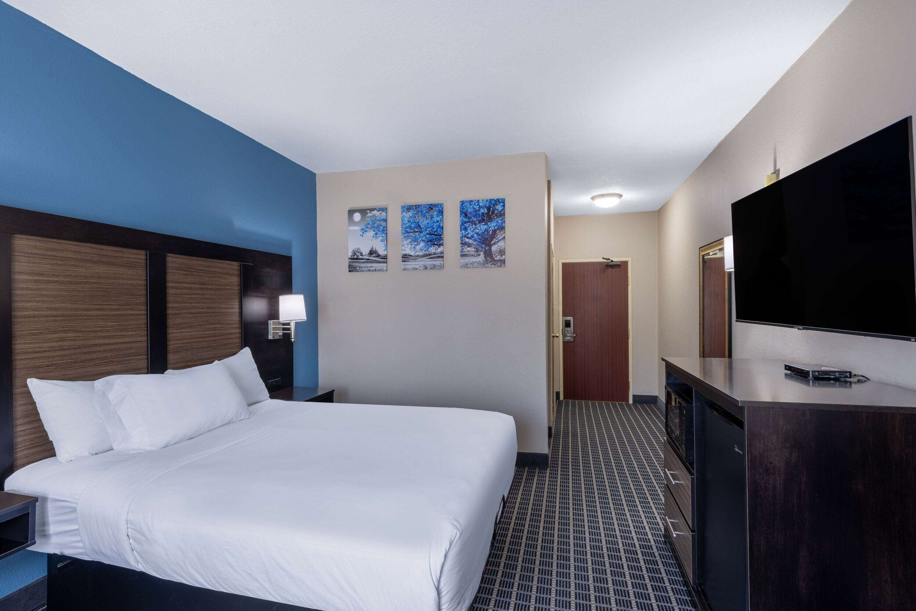 Habitación de hotel con una cama grande, un televisor de pantalla plana, un aparador y una puerta que da a un pasillo.