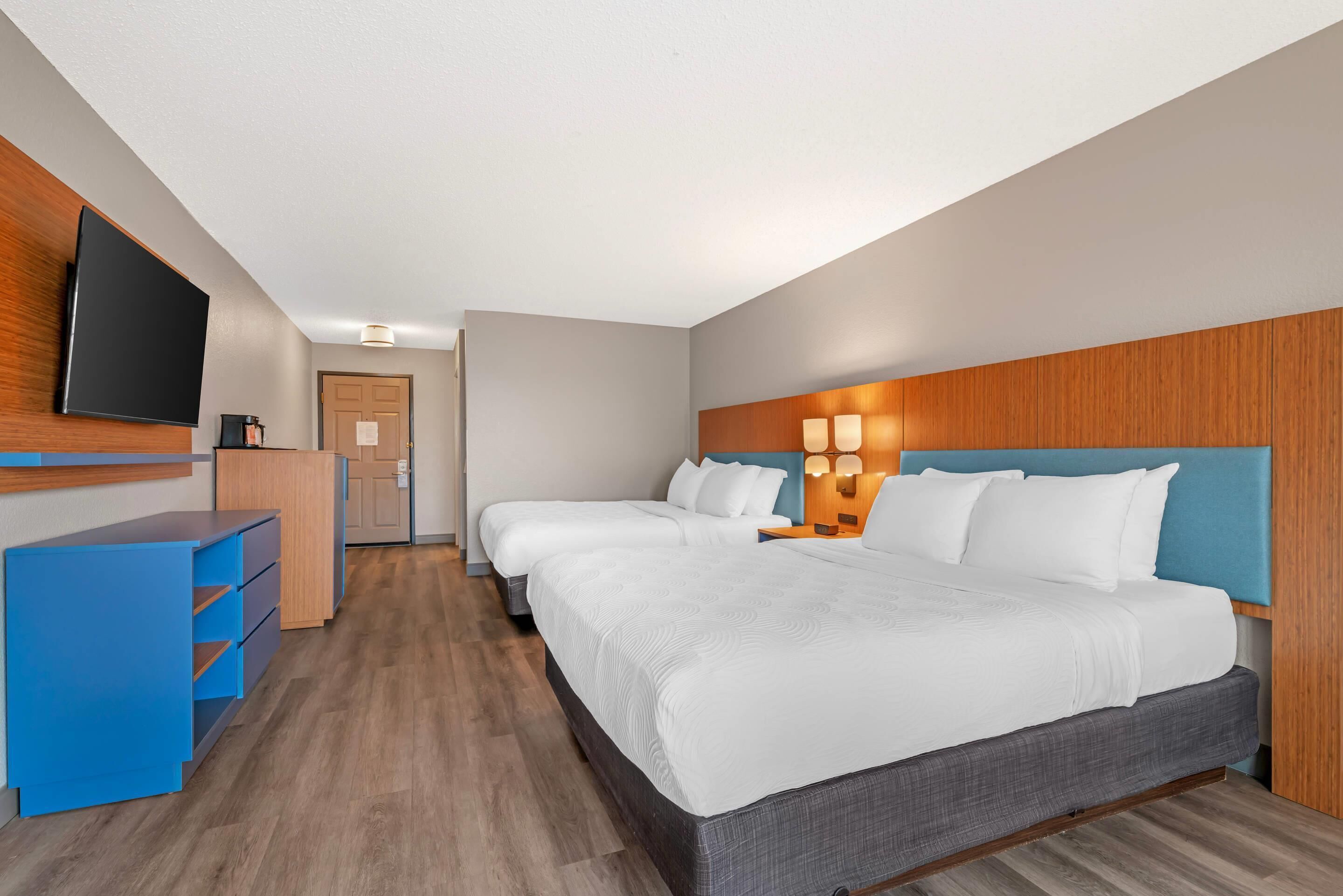 Une chambre d’hôtel avec un grand lit, une télévision, un bureau et une tête de lit en bois.