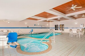 An indoor swimming pool with a blue chair, a sunbed, and a ceiling fan.