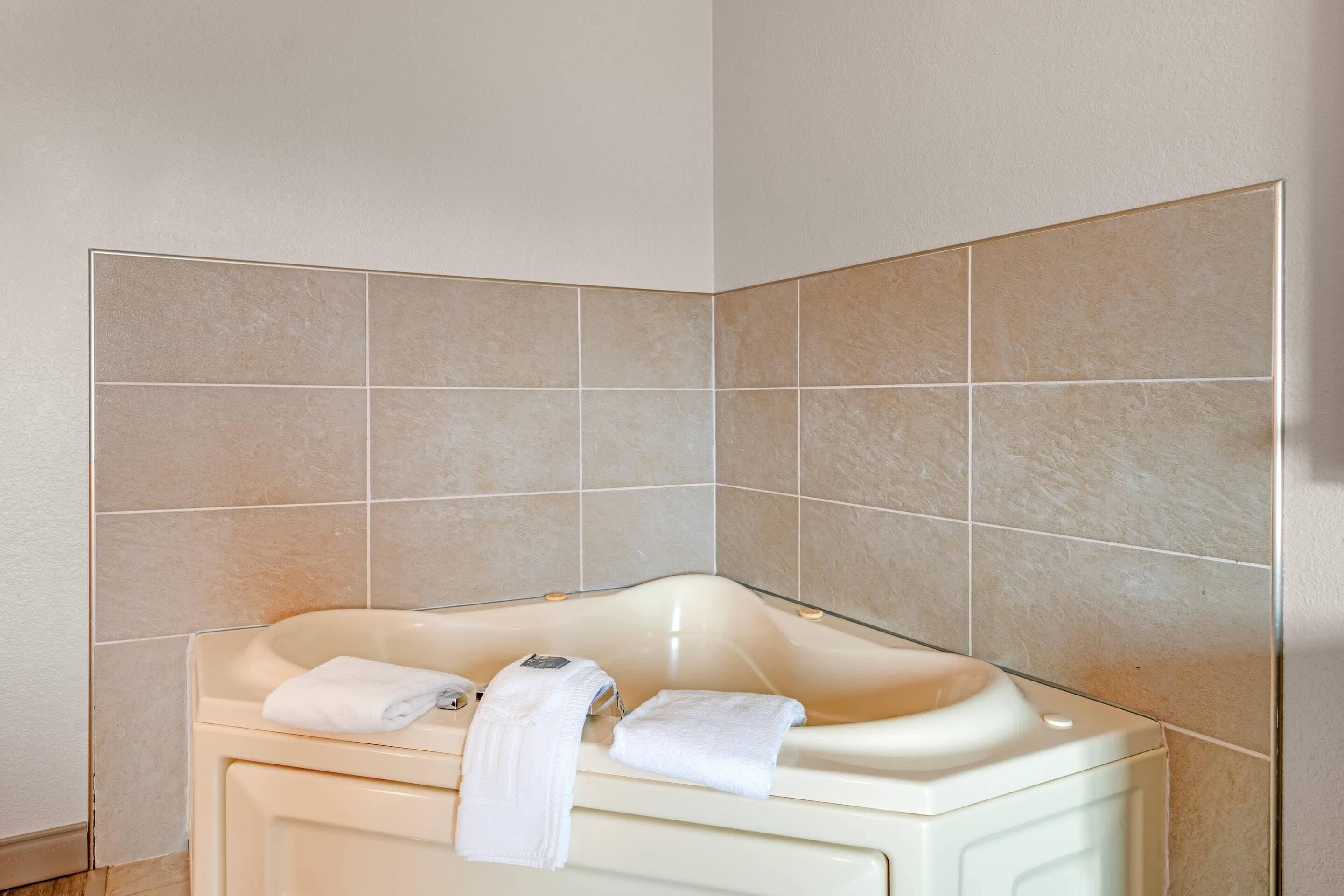 A corner bathroom with a bathtub, white towels, and beige tiles.