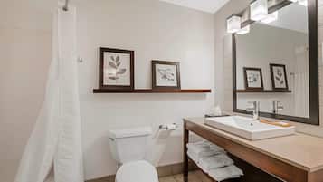 A bathroom with a white toilet, a sink with a mirror, framed pictures on the wall, and a shower curtain.