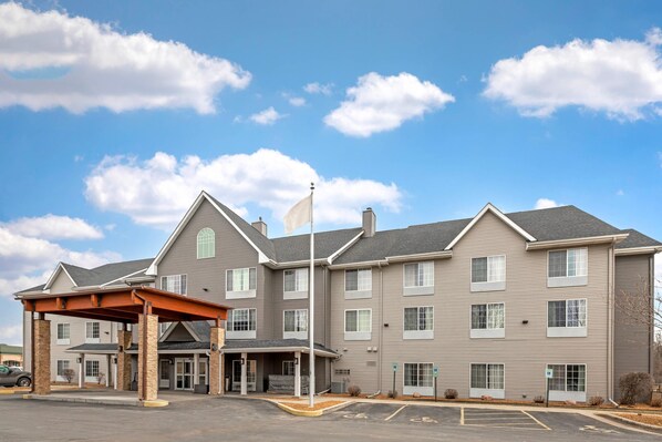 A multi-story hotel with a covered entrance, a flagpole, and a parking lot. - Country Inn & Suites by Radisson, West Bend, WI (West Bend)