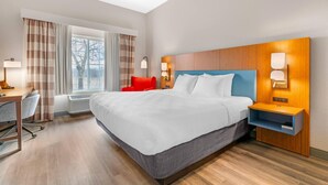 A hotel room with a large bed, a desk, a chair, a nightstand, and a window with curtains.