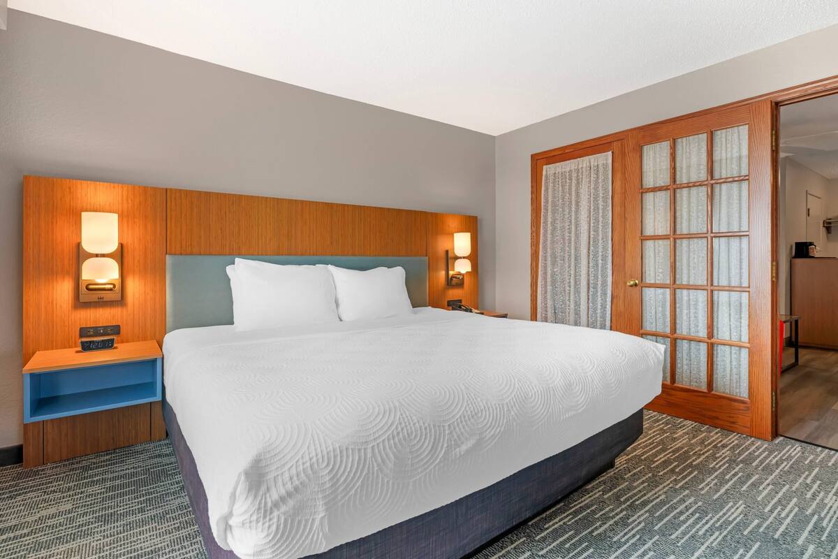 A hotel room with a large bed, wooden headboard, bedside lamps, and a door with frosted glass panels.