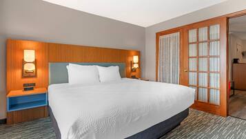 Habitación de hotel con una cama grande, cabecera de madera, lámparas de noche y una puerta con paneles de vidrio esmerilado.