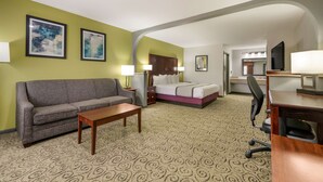 A hotel room with a gray sofa, a wooden coffee table, a bed with a white and pink bedspread, and a desk with a chair. - SureStay Hotel by Best Western Deer Park (Deer Park)