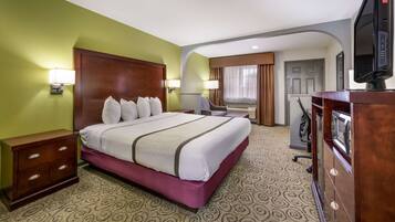 A hotel room with a large bed, a wooden dresser, a desk with a chair, and a television.