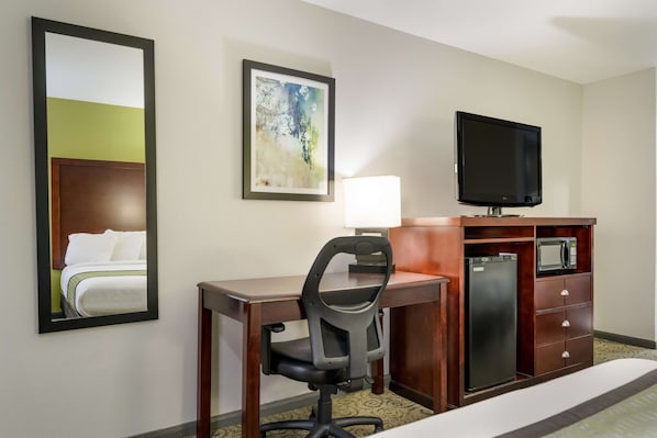 A hotel room with a bed, a desk with a chair, a television, a microwave, and a refrigerator.