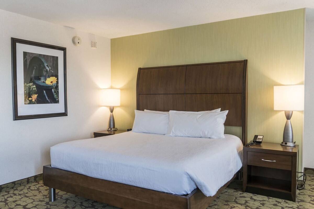 A hotel room with a bed, two bedside tables with lamps, a framed picture on the wall, and a patterned carpet.