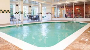 Piscina interna com água cristalina, rodeada por um deck ladrilhado e área de estar com cadeiras.