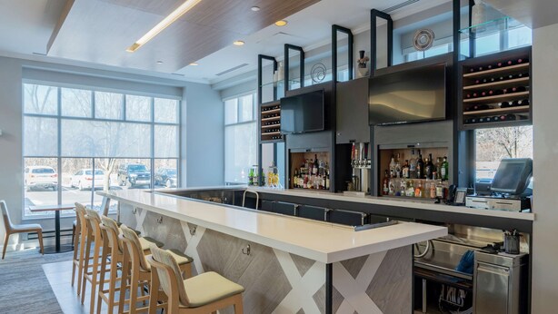 Uma área de bar moderna com um balcão comprido, banquetas e prateleiras cheias de garrafas.
