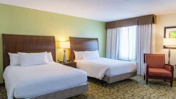A hotel room with two beds, a chair, and a window with curtains.