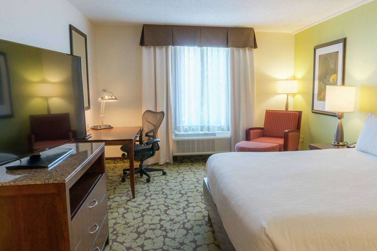 A hotel room with a bed, desk, chair, TV, and a window with curtains.
