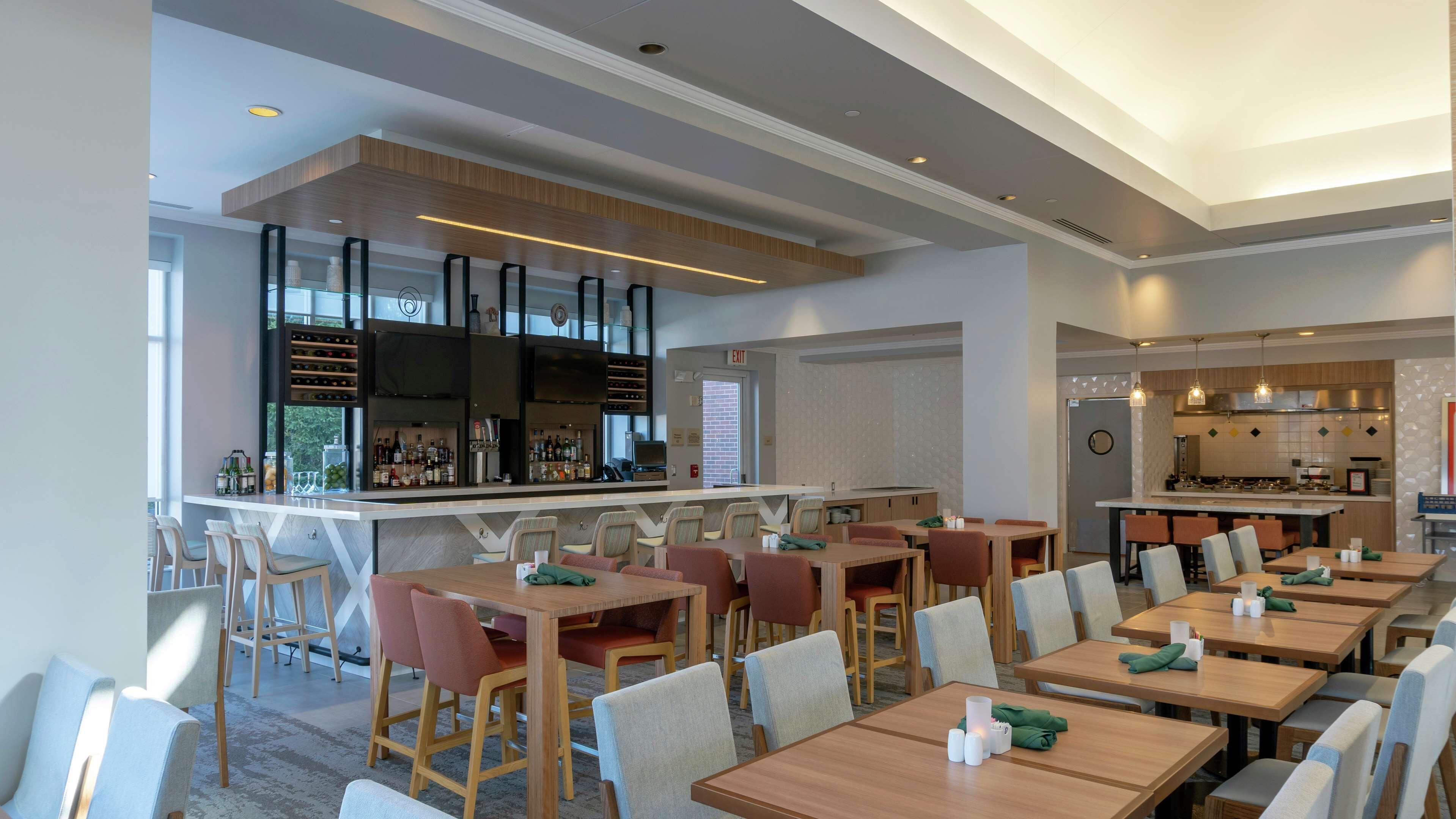 A modern restaurant with multiple dining areas, a bar, and a kitchen visible in the background.