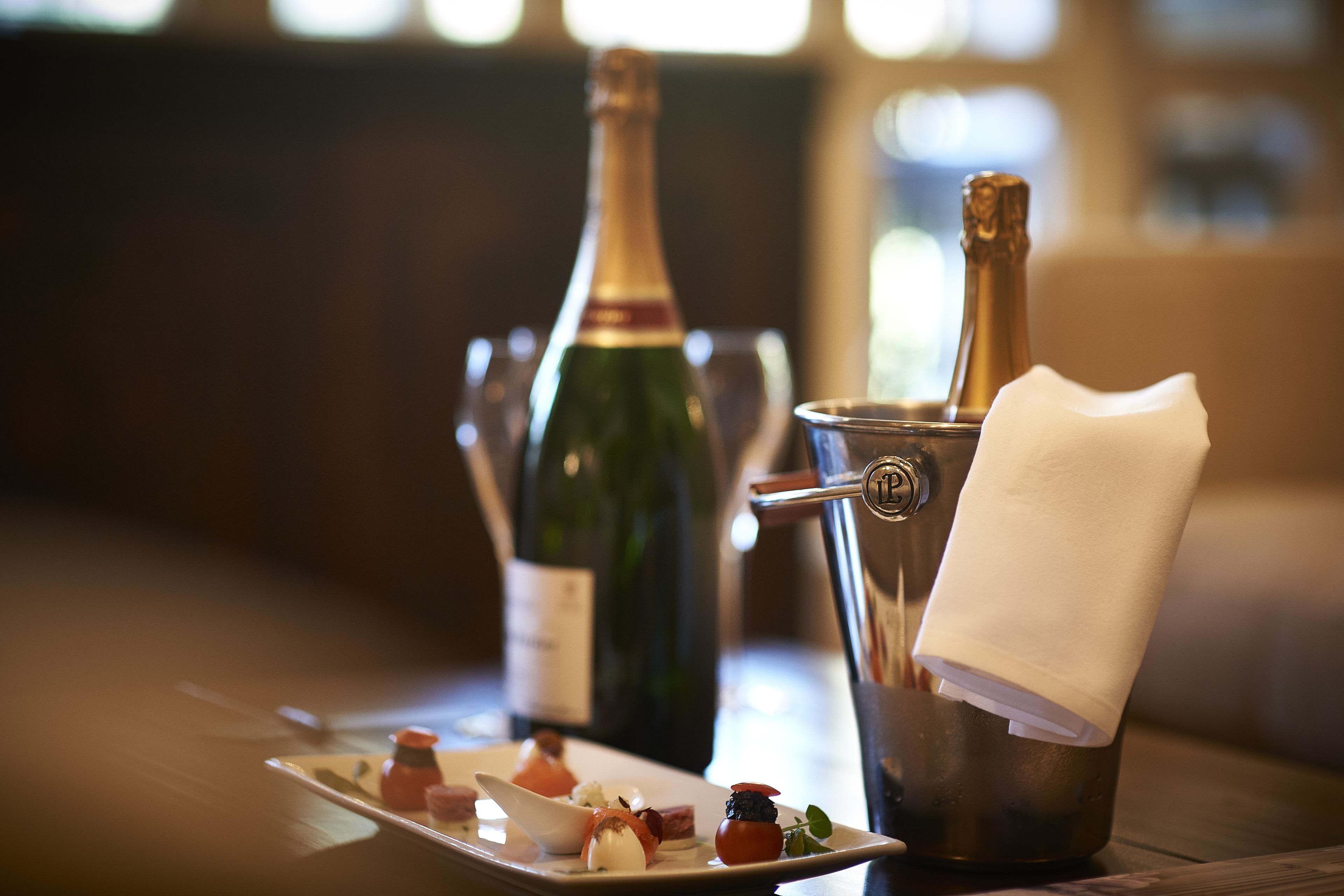 A table with a bottle of champagne, a glass, and a plate of appetizers.