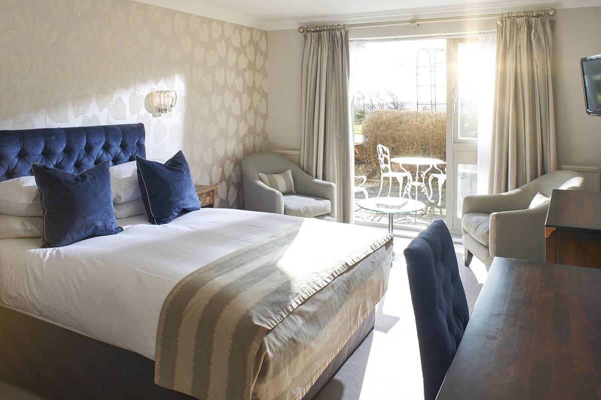 A hotel room with a large bed, two armchairs, a small table, and a view of the garden through the window.