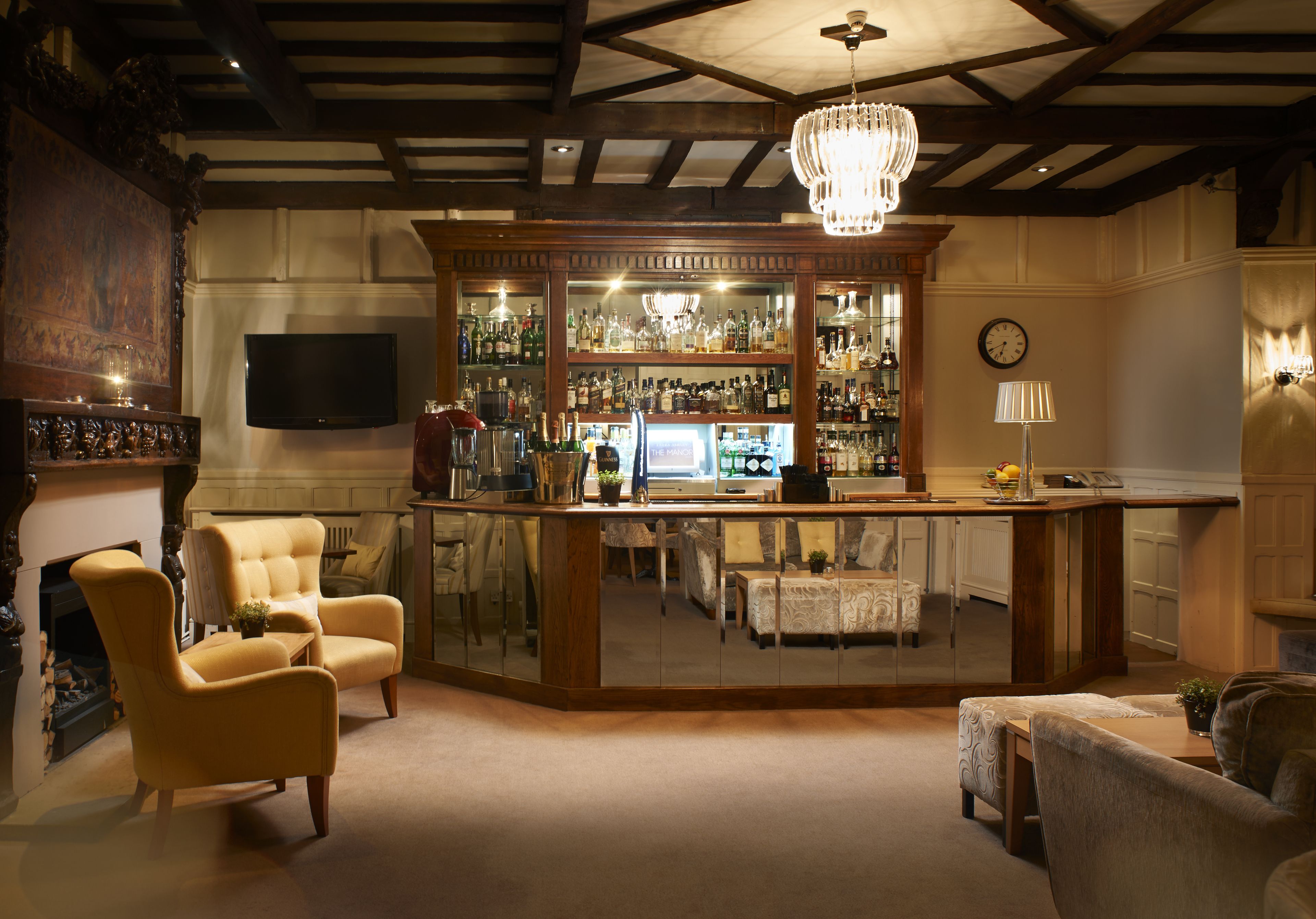 A bar area with a wooden counter, a television mounted on the wall, and a chandelier.